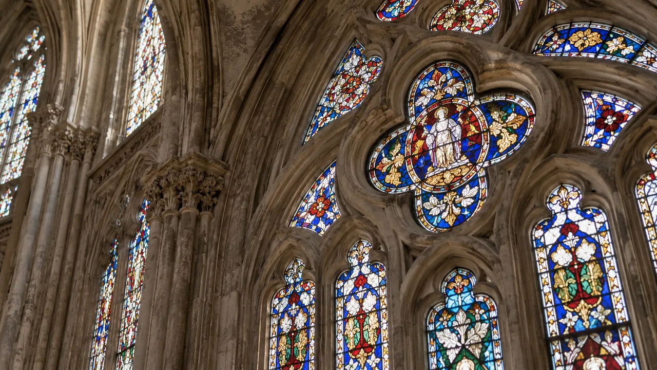 Ventana de vidriera enmarcada por tracería de piedra de estilo gótico.